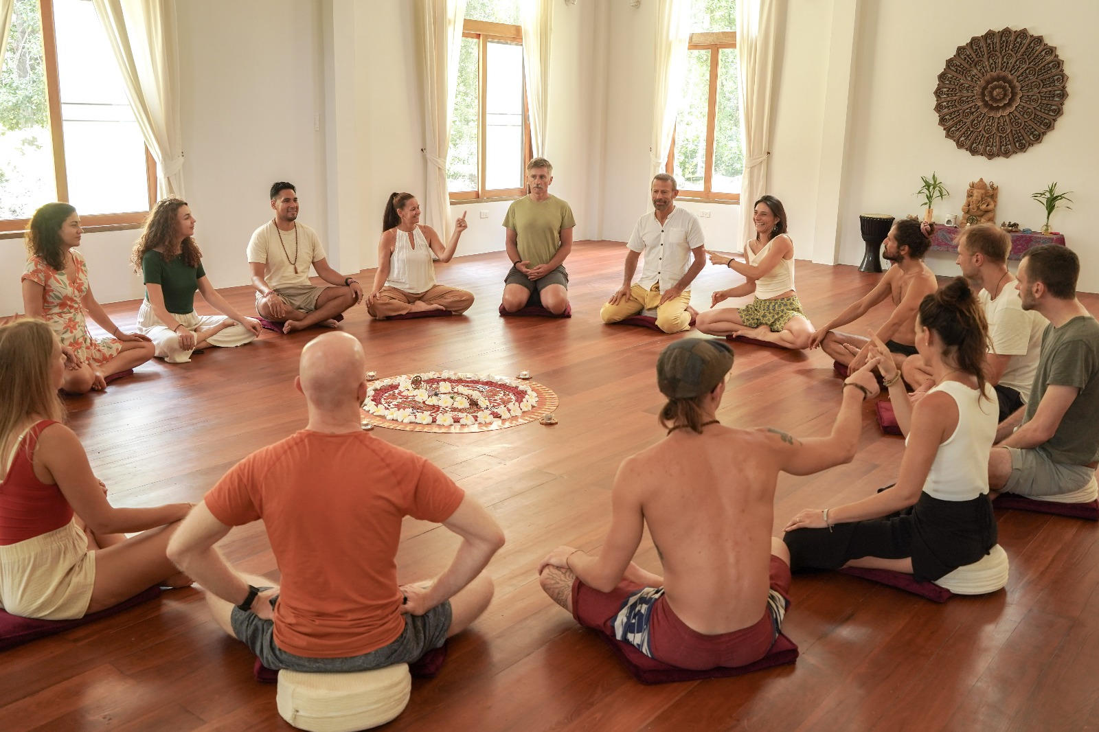 A group of people sitting on cushions and mats in a bright, plant-filled studio during a breathwork session